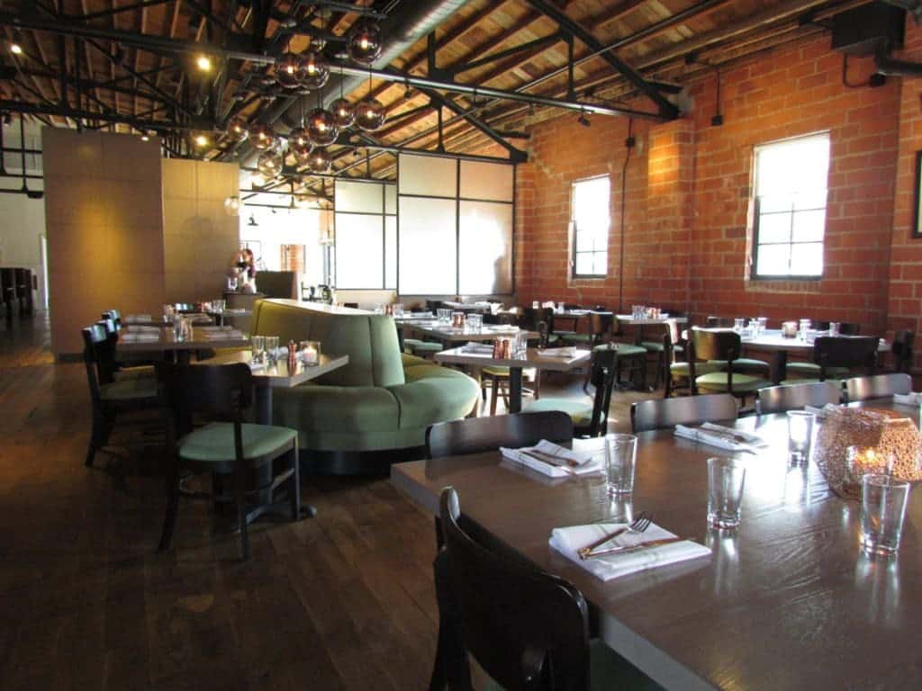 Stark tables and plush booth seating offer the seating options at Third Street Social. High wood beam celiengs rise above the indutrial style interior.