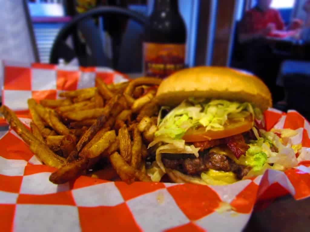 The grass fed burgers are piled high with lettuce, pickles, and tomatoes. Spicy french fries round out the basket of food in one of Tay's Burger Shack's value meals.
