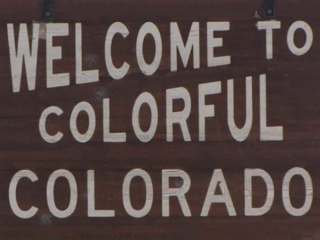 Bright white stenciled letters on a dark brown sign denote to travelers "Welcome To Colorful Colorado".