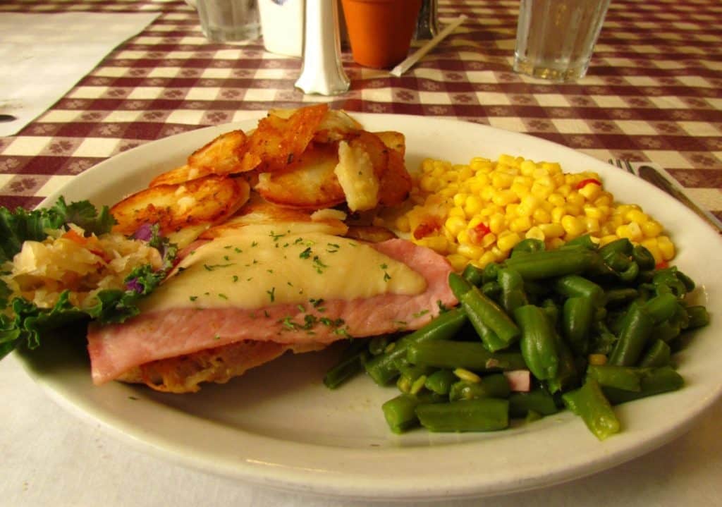 A ham and Swiss covered chicken breast with potatoes and vegetables.