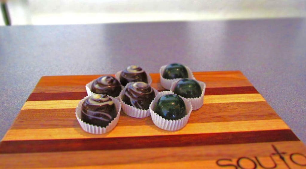 Samples of two varieties of artisan chocolates are served on a wooden tray.