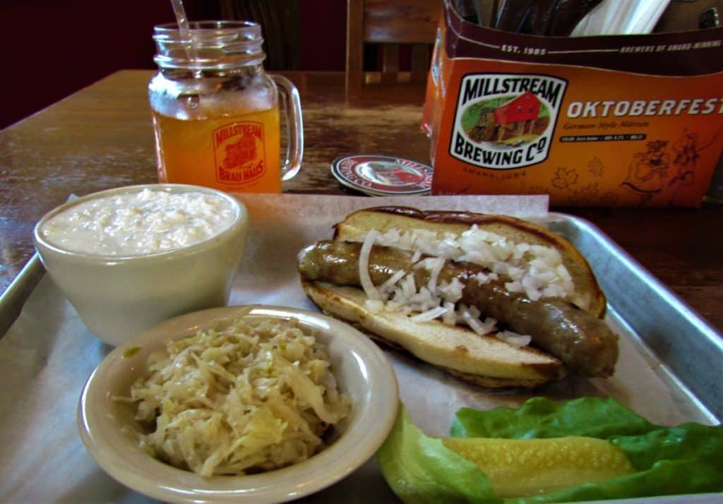 A German Bratwurste is served with fresh sauerkraut. The meal is accompanied by a bowl of cottage cheese, and a mug of orange soda.