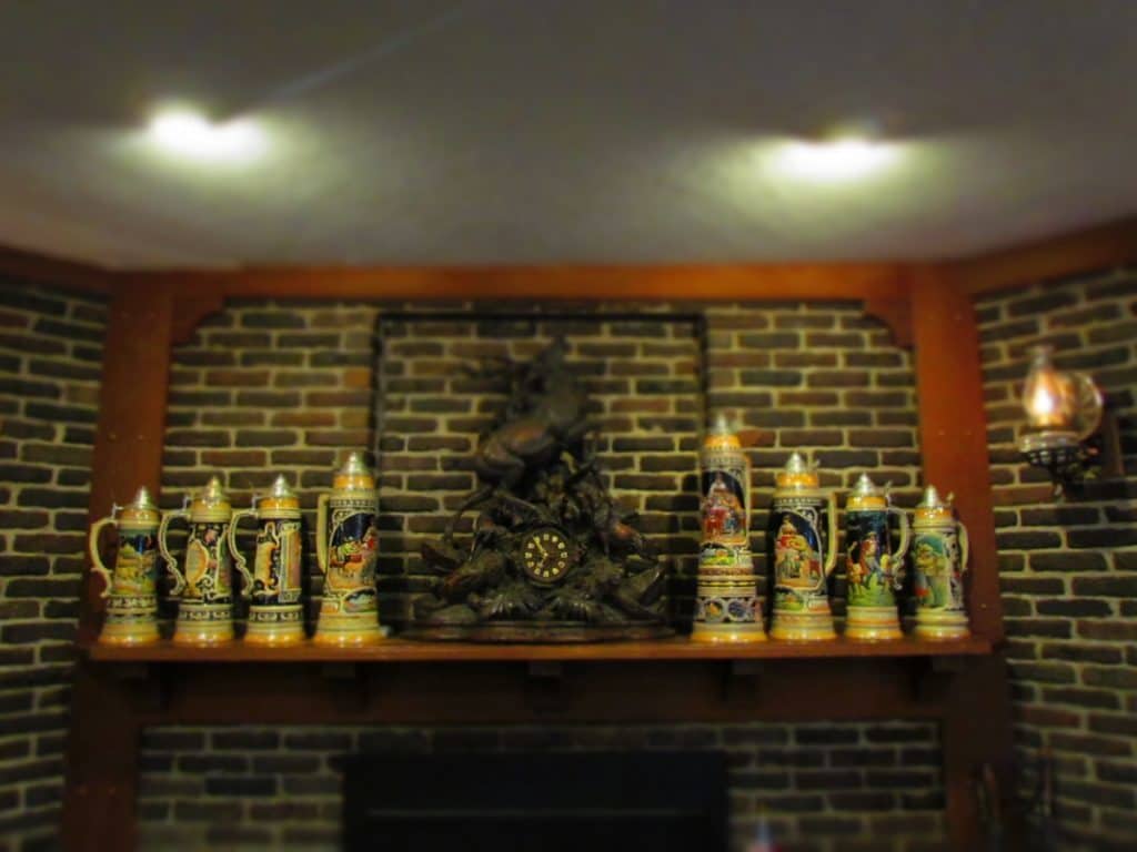 An over-sized mantel clock and various German beer steins adorn the wooden fireplace mantel.