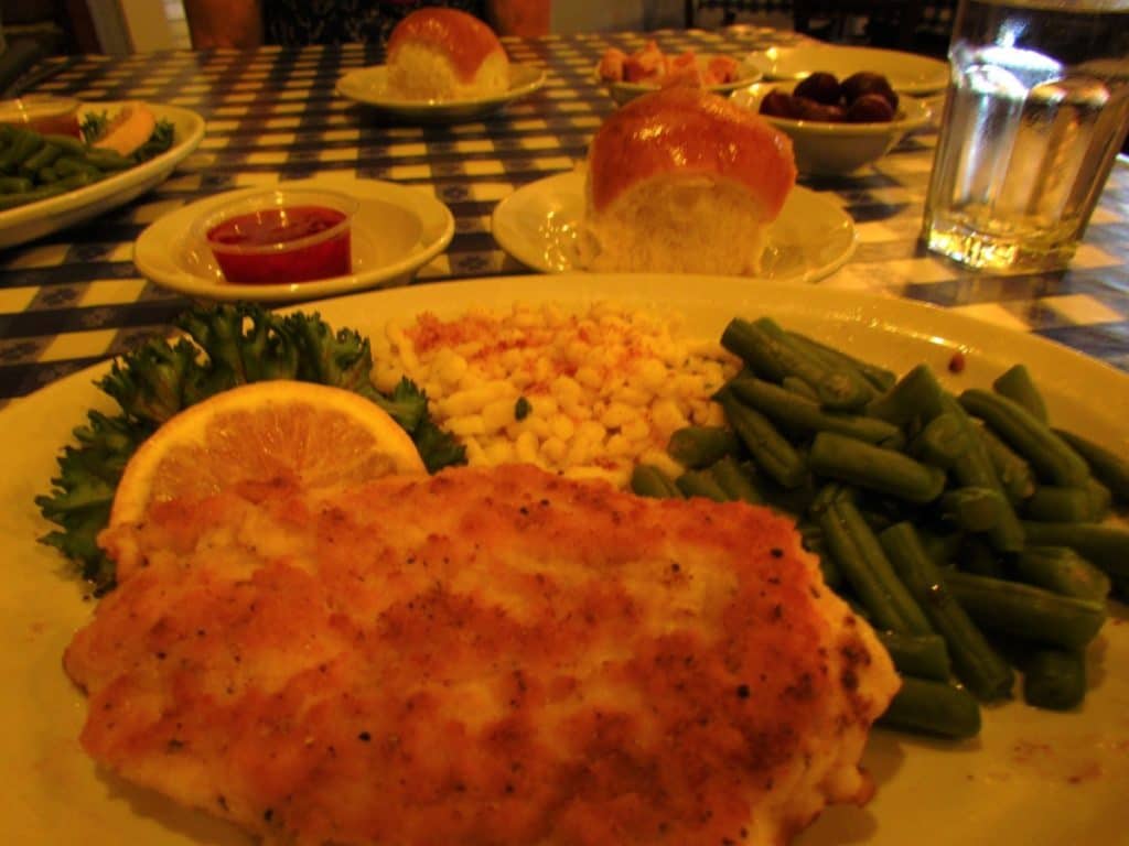 A dinner plate filled with Chicken Schnitzel, green beans, sweet corn, and served with a homemade roll with strawberry jam.