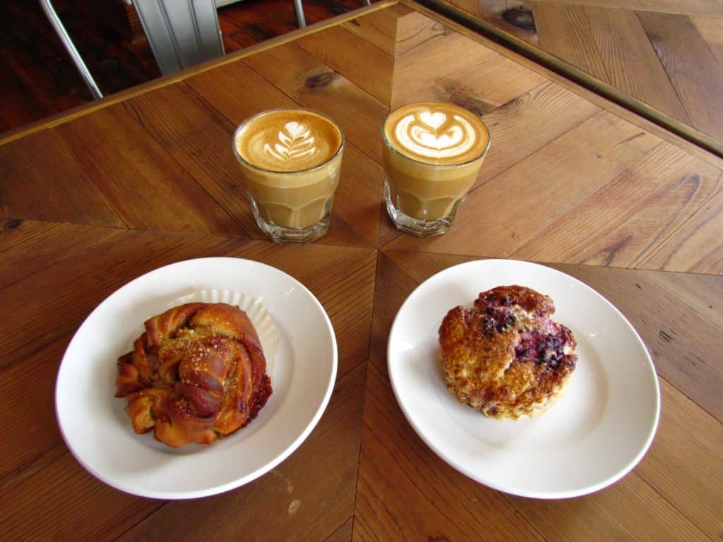 Pastries and coffees are displayed on a par quay wooden table top.