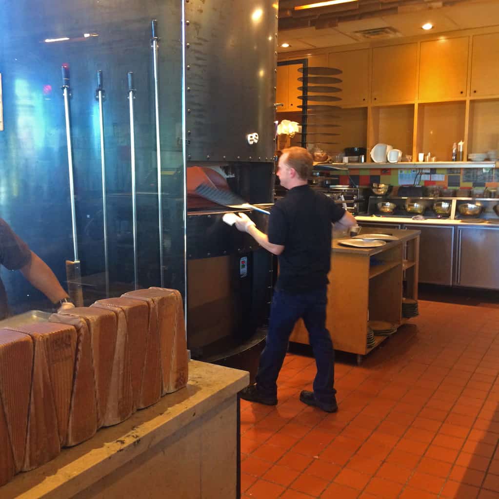 A staff member checks the pizza pies in the wood fired oven at Spin Pizza.