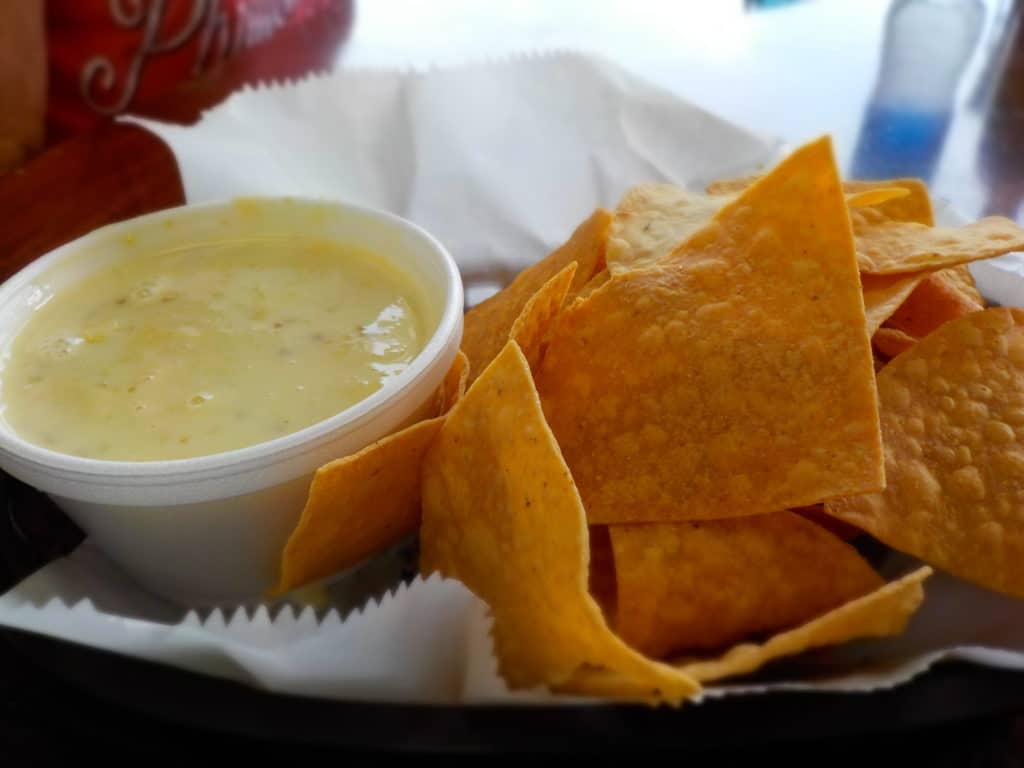 A bowl of Queso cheese dip is served with crispy tortilla chips.