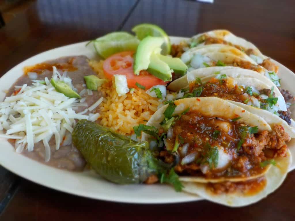 A plate filled with street tacos also holds refried beans and rice.