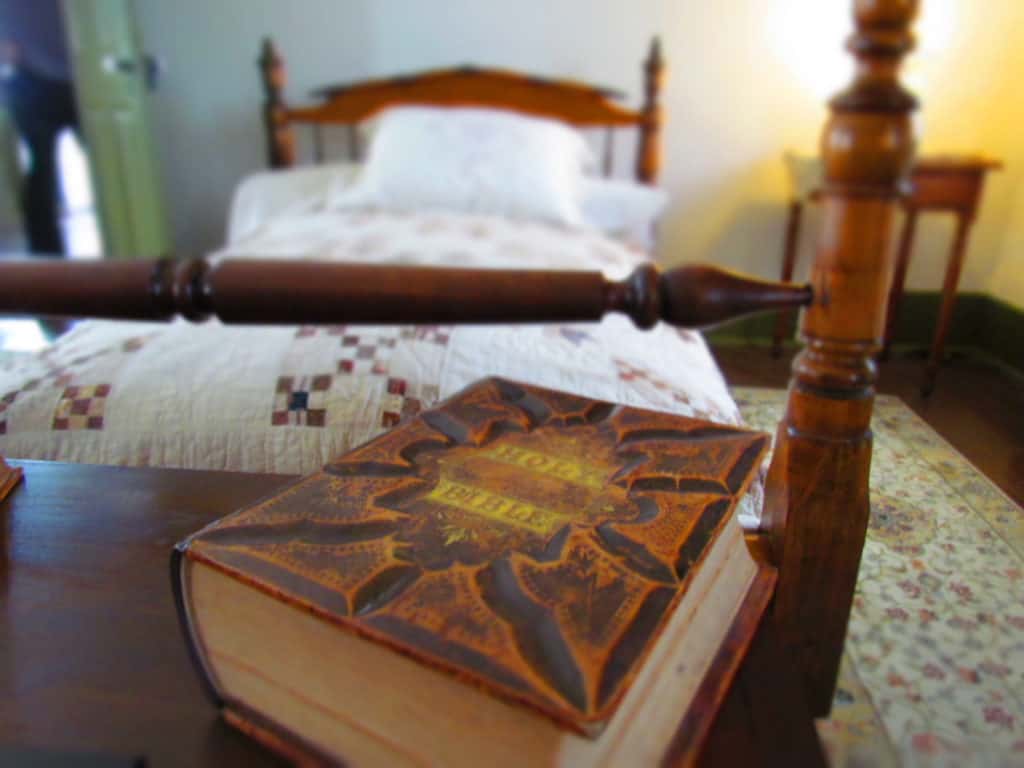 A bible rest on a chest at the foot of a bed.