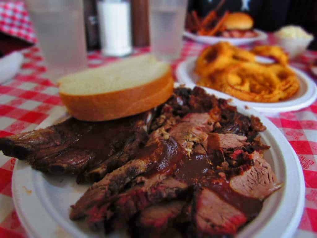 Combo platter featuring ribs, burnt ends, chicken, and sliced beef brisket is accompanied by a side order of crispy onion rings. 