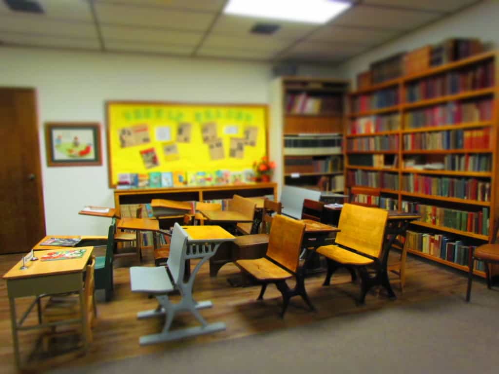 A recreated school classroom is filled with a variety of old school desks. 