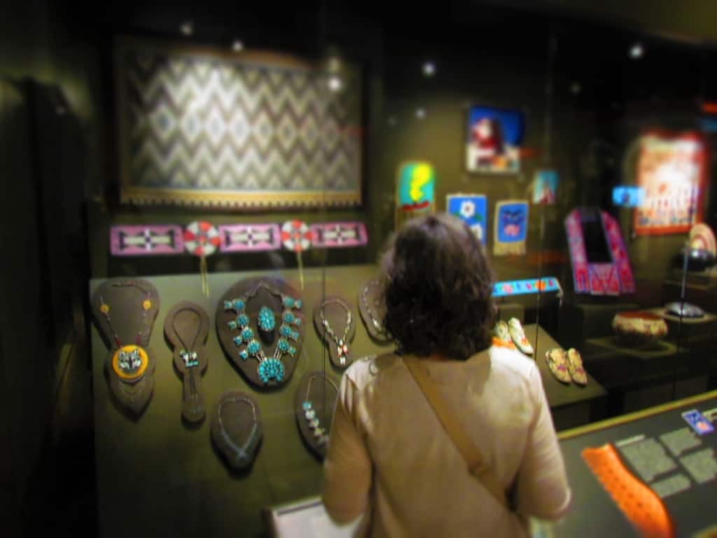 The author poses in front of a display of Native American jewelry and beadwork pieces. 