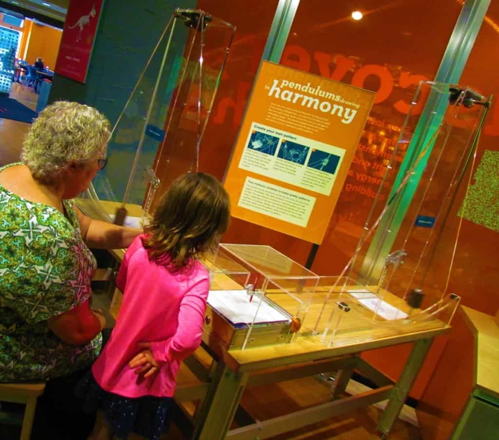 Tow museum patrons take a turn at the pendulum to create a one of a kind piece of art. 