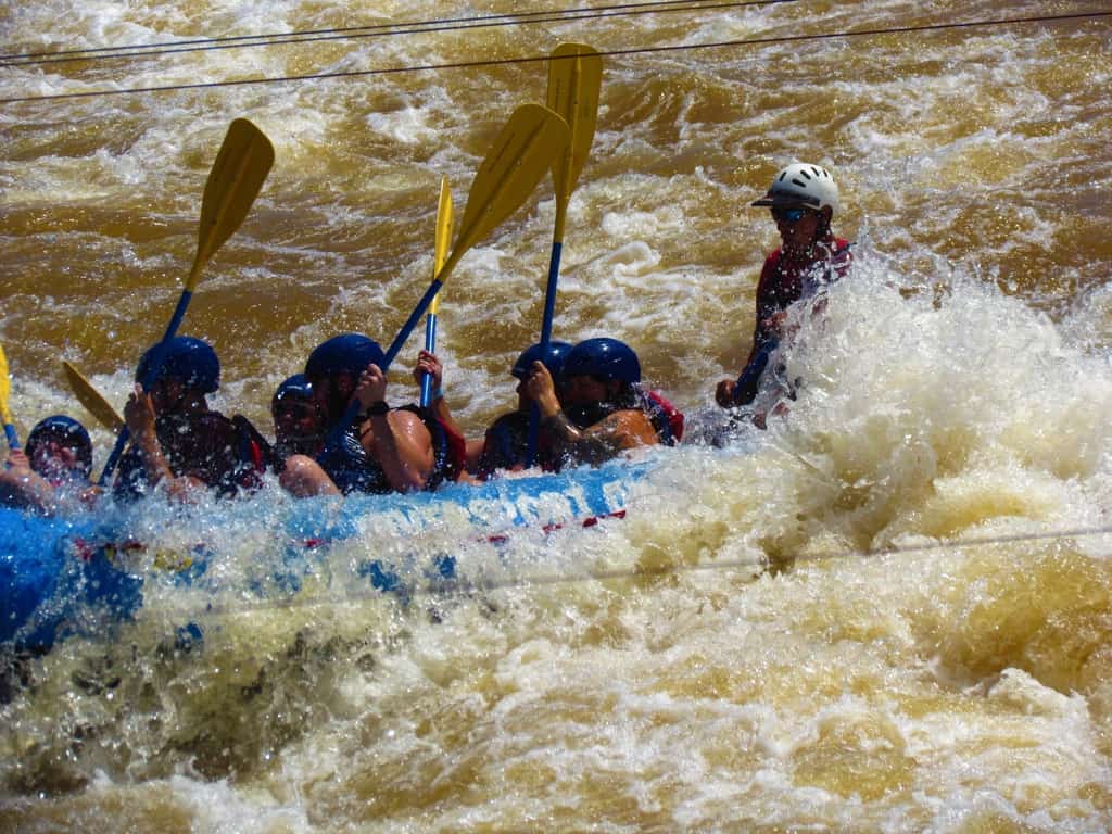 A boat team gets drenched as they hit a turbulent spot in the river.
