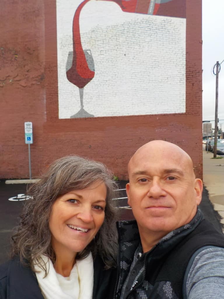 The authors pose in front of a wine mural in Kansas City, Missouri Crossroads District. 