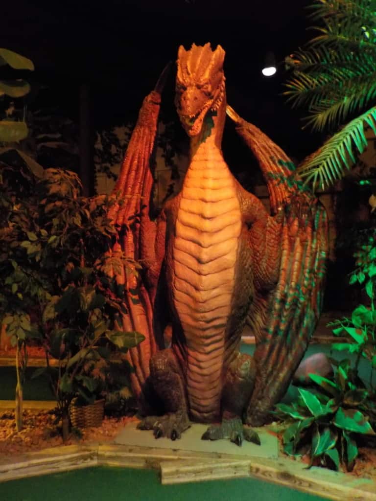 A scary dragon stands watch over one of the holes at an indoor mini-golf course.