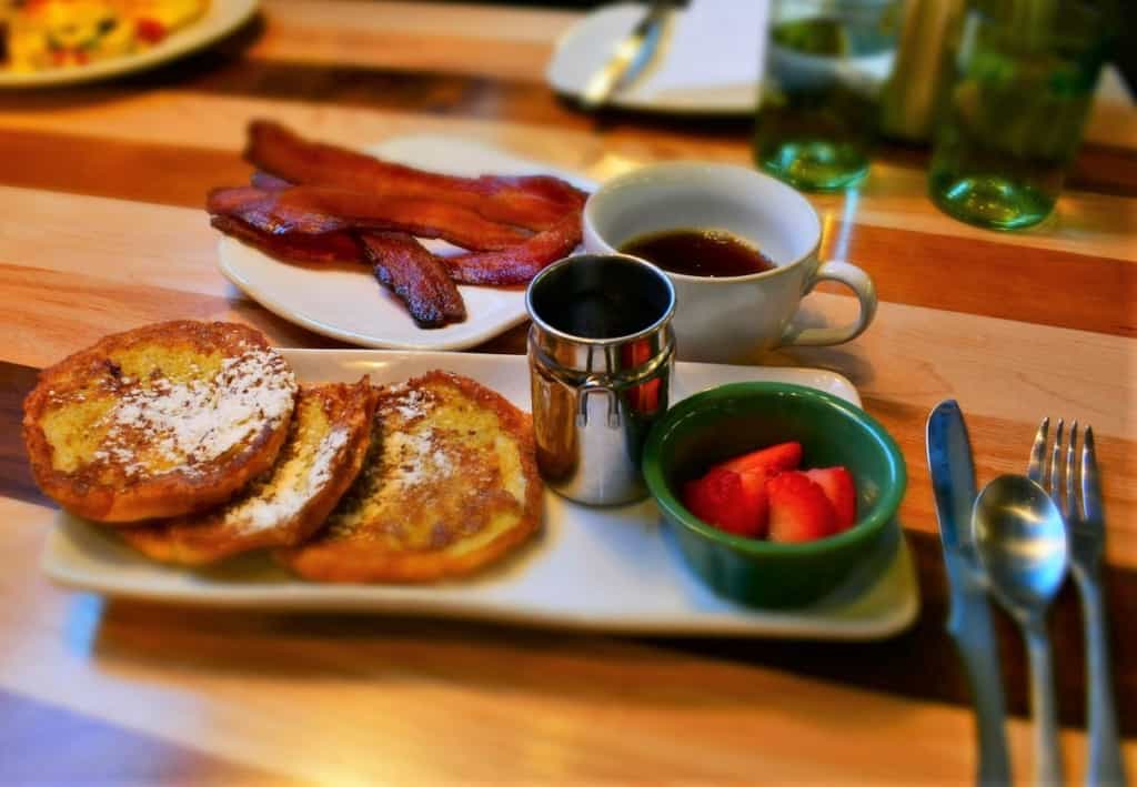 A plate of Croissant French Toast is accompanied by thick cut bacon. 